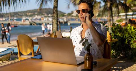 Zakenman zit op het strand achter zijn laptop en is aan het bellen